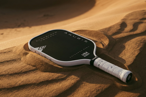 Pickleball paddle on sand with 'ANUBIS' branding. Made in Aotearoa